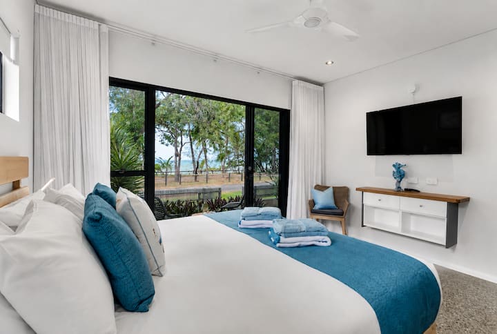 Manta Room master bedroom with a king bed and glass doors to a private patio, with trees and a glimpse of the sea beyond.