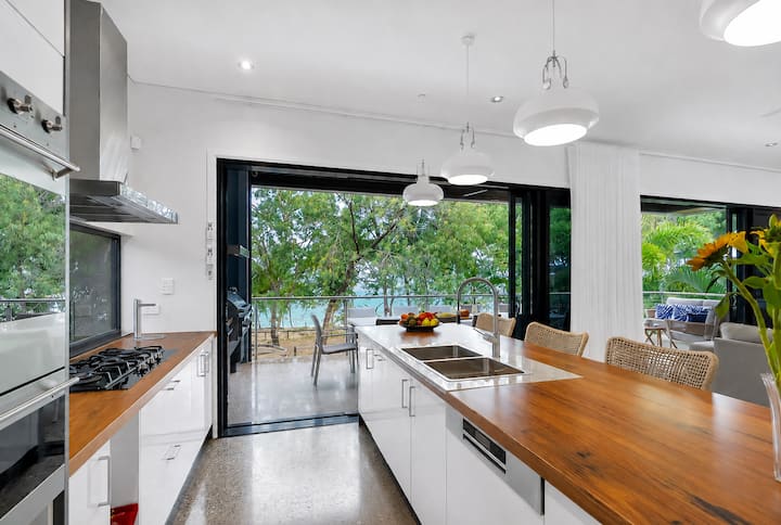 Long kitchen bench with gas cooktop, looking through glass doors to the balcony and the sea.