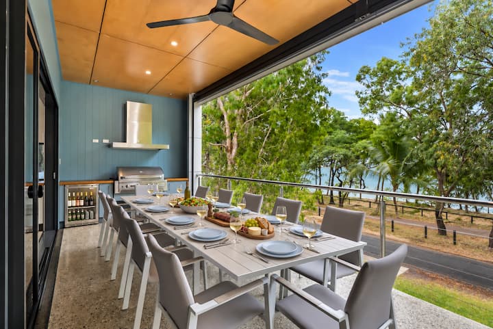 Long outdoor dining table on the covered balcony, looking through the foreshore trees to the sea.