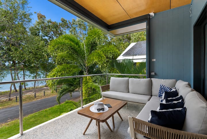 Outdoor lounge on the elevated balcony, with palms and the foreshore beyond.