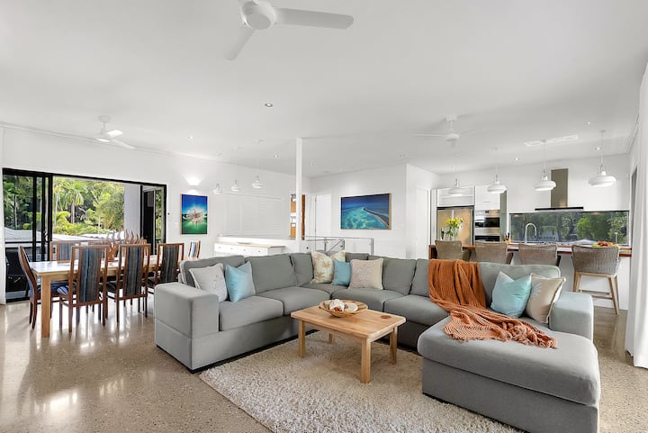Open-plan living room with a large sofa, dining table and kitchen beyond.