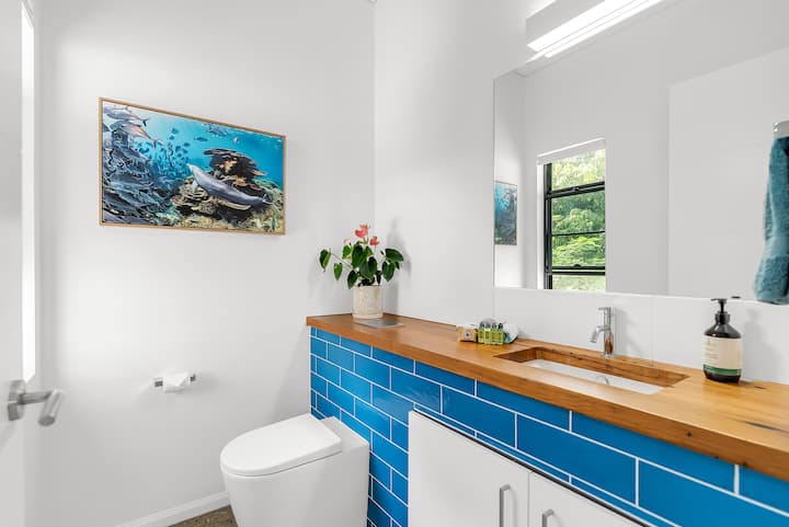Upstairs room with a toilet, blue-tiled vanity and reef photography, beside the bunk room.