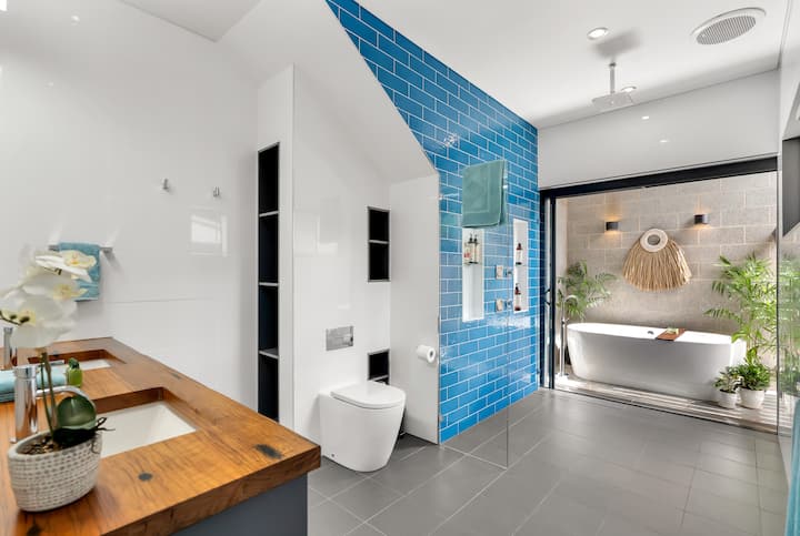 Master ensuite with timber vanity, blue-tiled wall and freestanding bath.