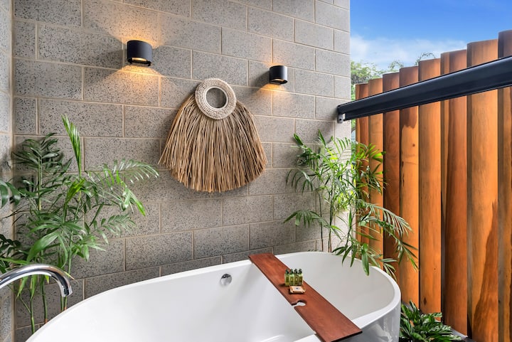 Freestanding bath in the master ensuite with a timber bath caddy and tropical plants.