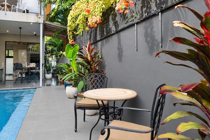 Poolside courtyard with a small table and chairs among tropical plants.