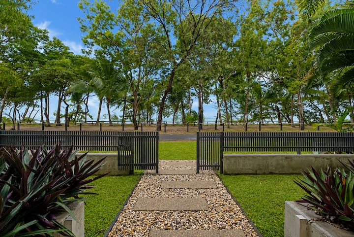 View from the front path through the gate: the quiet road, then foreshore trees and the sea.
